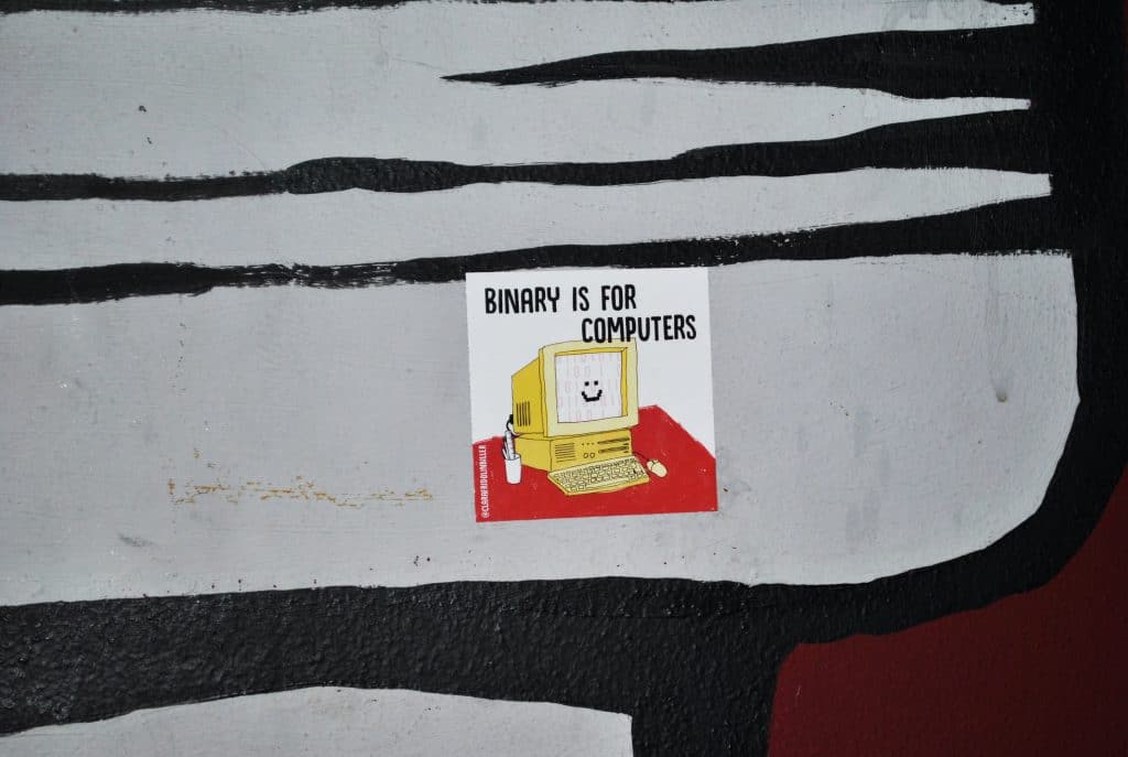 A sticker on a patterned wall that says "Binary is for Computers", with an illustration of as smiling yellow computer