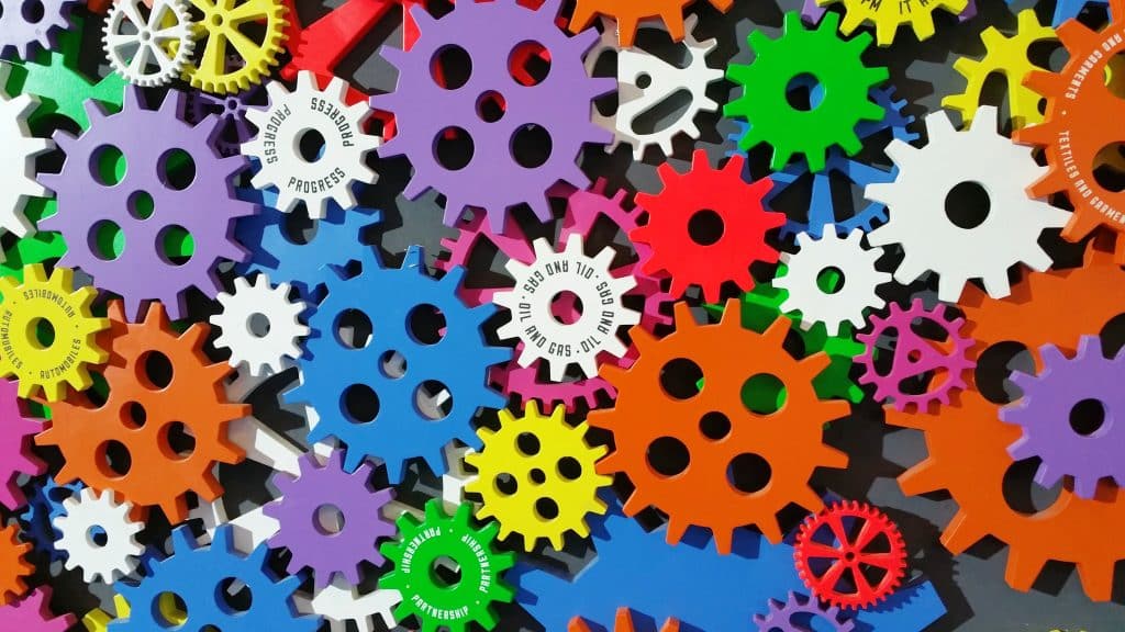 A colourful display of plastic cog wheels laid on top of each other in a seemingly endless pile. It is bright, colourful, and chaotic all at once.