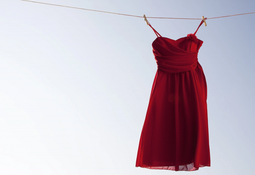 An image symbolizing Red Dress Day. A vibrant red dress hangs alone on a clothesline against a bright, clear sky symbolizing Red Dress Day