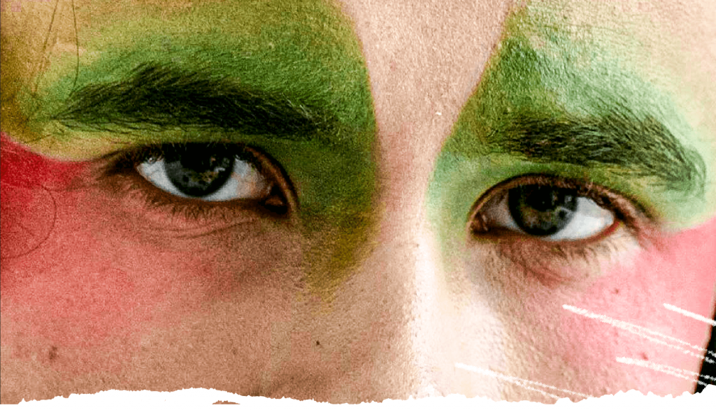 Close-up of male-presenting eyes with light red and green make-up.